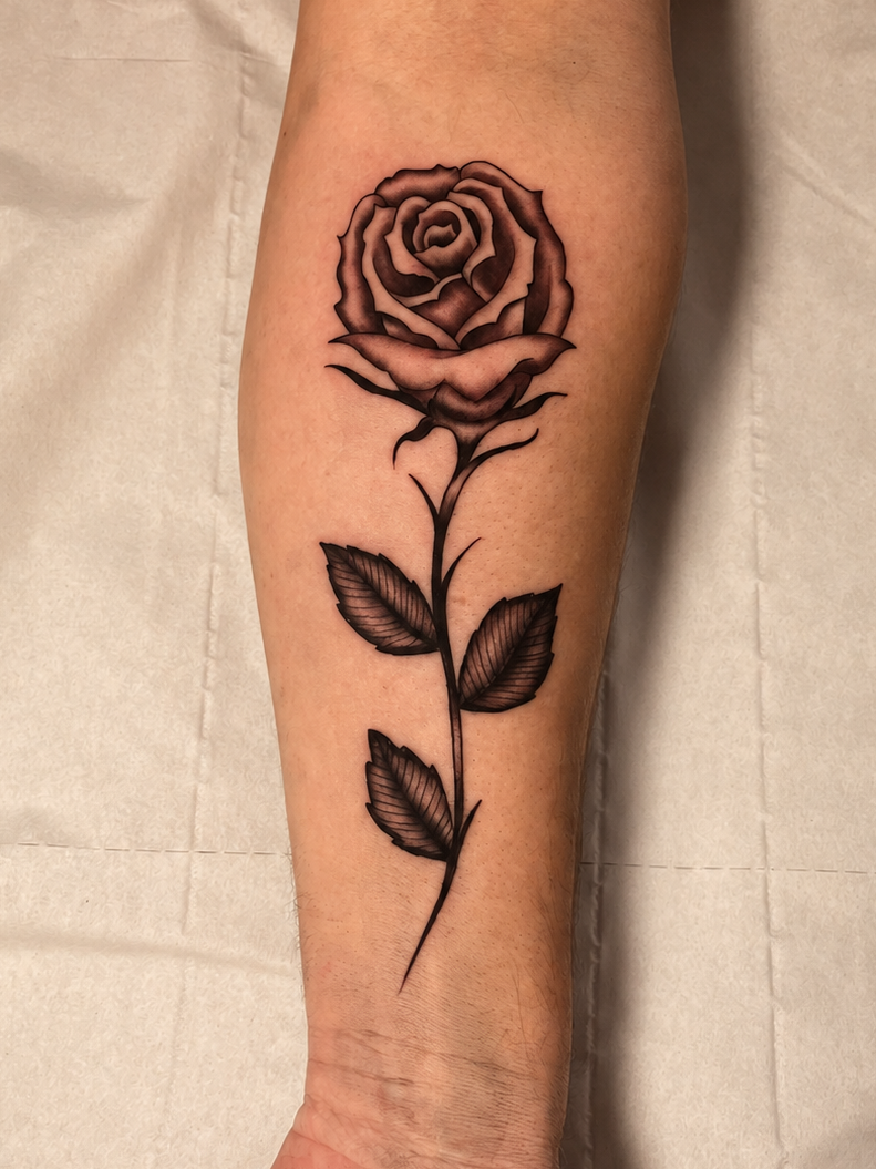 A black and gray rose tattoo on a person's forearm, shown against a light beige fabric background.